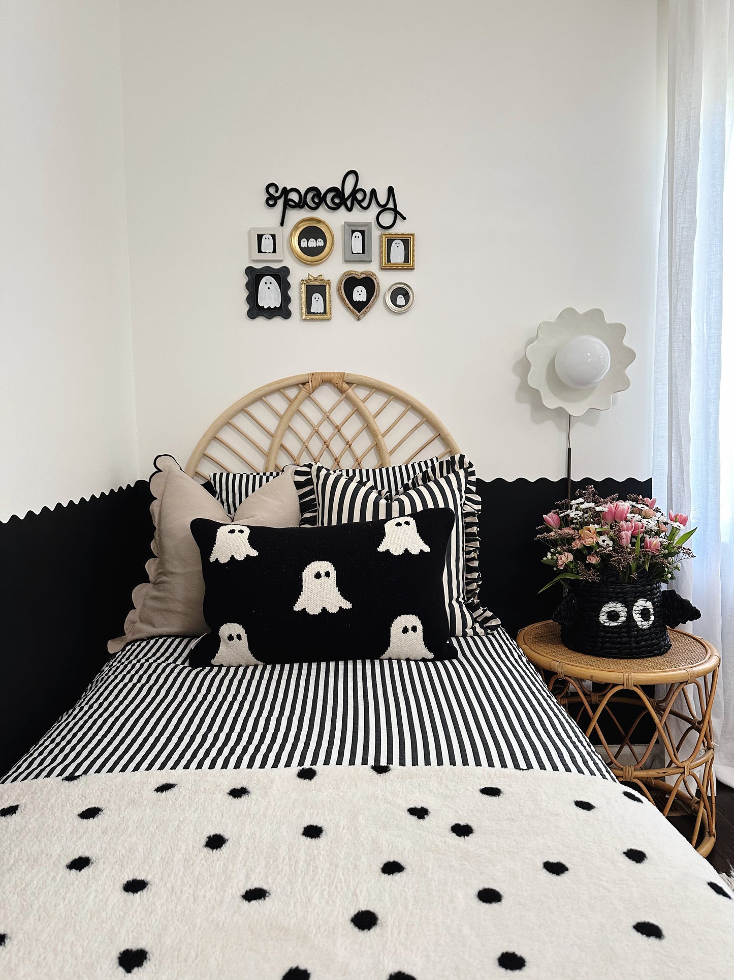 Black knitted wire ‘Spooky’ sign above a black-and-white ghost gallery wall in a boy’s bedroom. Room features a woven headboard, striped pillows, a ghost-themed pillow on the bed, and a black bat woven basket with flowers on the nightstand, creating a playful and festive Halloween vibe.