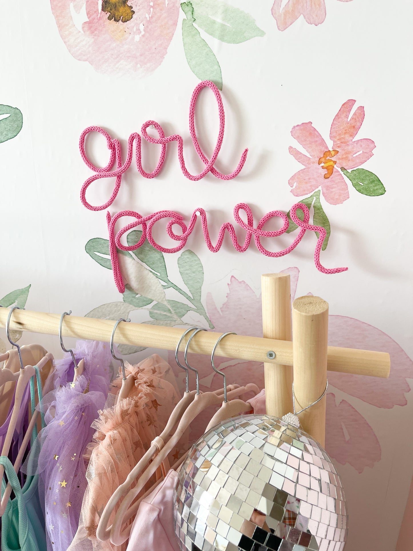 knitted wire word "girl power". It's hanging above a dress up rack in a girls bedroom.