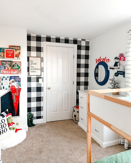 Red ‘Ho Ho Ho’ knitted wire word above a mirror in a boy’s room, showing bookshelves with holiday books, white and black check wallpaper, and festive Christmas décor with red accents.