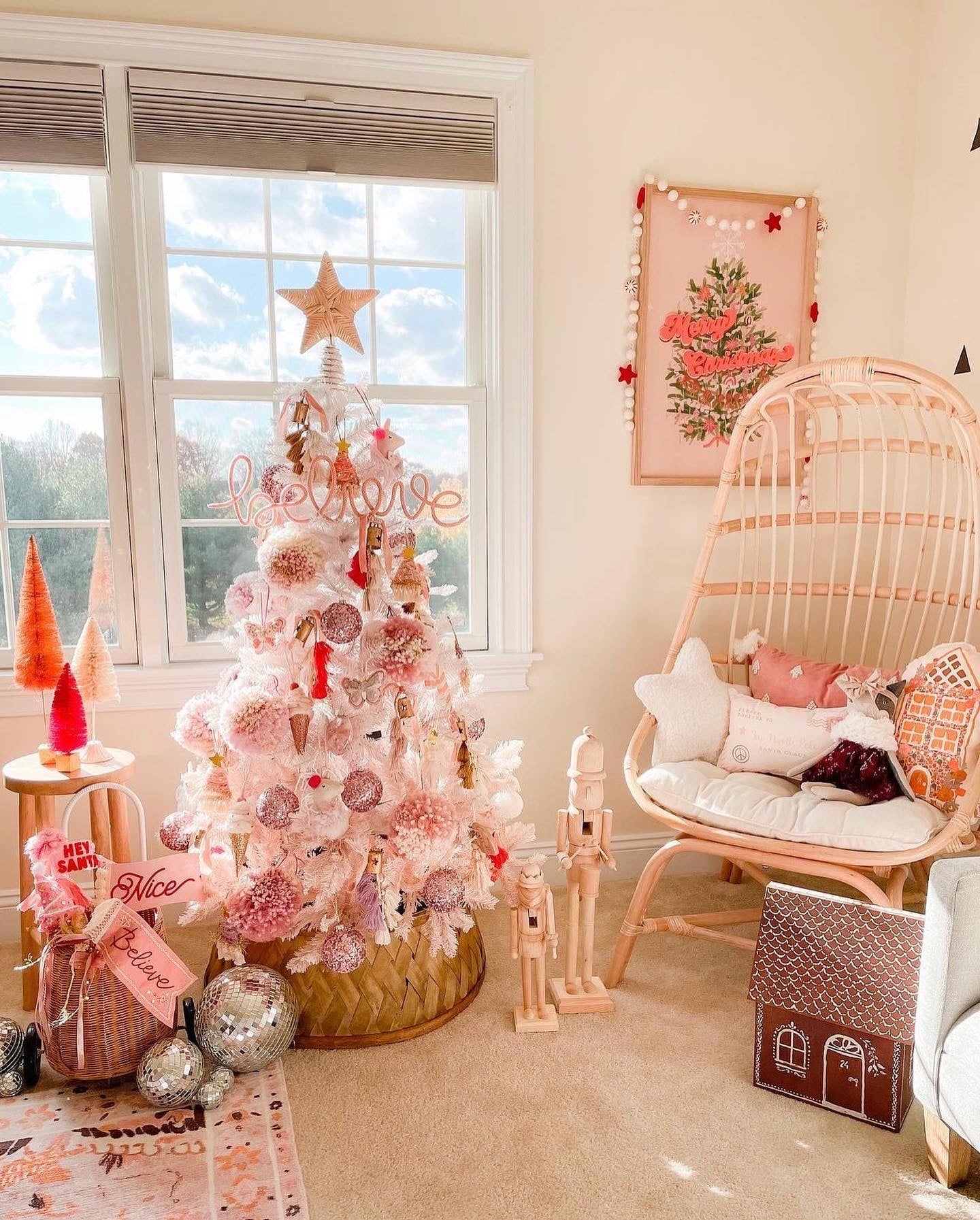 Little girl’s room decorated for Christmas with blush pink decor. Pink ‘Believe’ knitted wire sign displayed in the tree, pink tree artwork with garland, pink and red bottle brush trees, wooden nutcrackers, and disco balls.