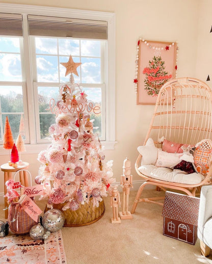 Little girl’s room decorated for Christmas with blush pink decor. Pink ‘Believe’ knitted wire sign displayed in the tree, pink tree artwork with garland, pink and red bottle brush trees, wooden nutcrackers, and disco balls.