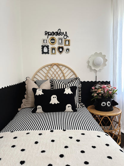 Black knitted wire ‘Spooky’ sign above a black-and-white ghost gallery wall in a boy’s bedroom. Room features a woven headboard, striped pillows, a ghost-themed pillow on the bed, and a black bat woven basket with flowers on the nightstand, creating a playful and festive Halloween vibe.