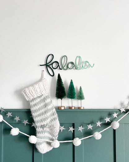 Green to mint ombre fa la la knitted wire word sign on wall with stocking, bottle brush trees and garlands.