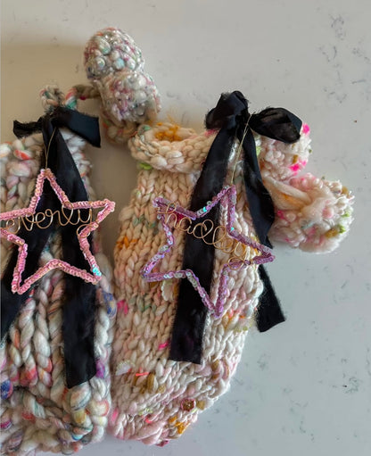 Two cozy handmade Christmas stockings with personalized sequin star ornaments as stocking tags - a pink star for Hadley and a purple star for Everly, whimsical holiday decor.