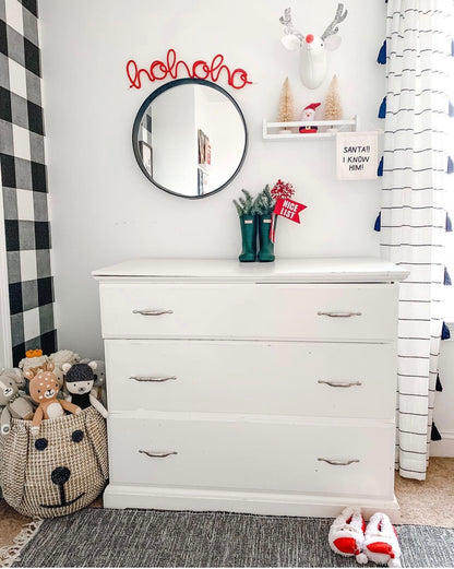 Red ‘Ho Ho Ho’ knitted wire word displayed over a mirror in a boy’s room, featuring whimsical Scandi-style Rudolph wall mount, white and natural accents, and green and red decor.