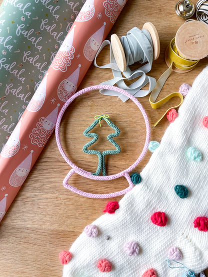 A handcrafted snow globe tree-shaped, placed on a textured surface with various crafting materials around it.