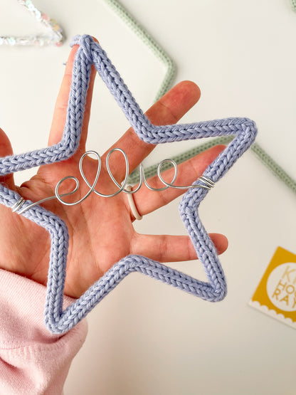 Hand holding periwinkle colored knitted wire star ornament personalized with name 'ellie' in silver wire.