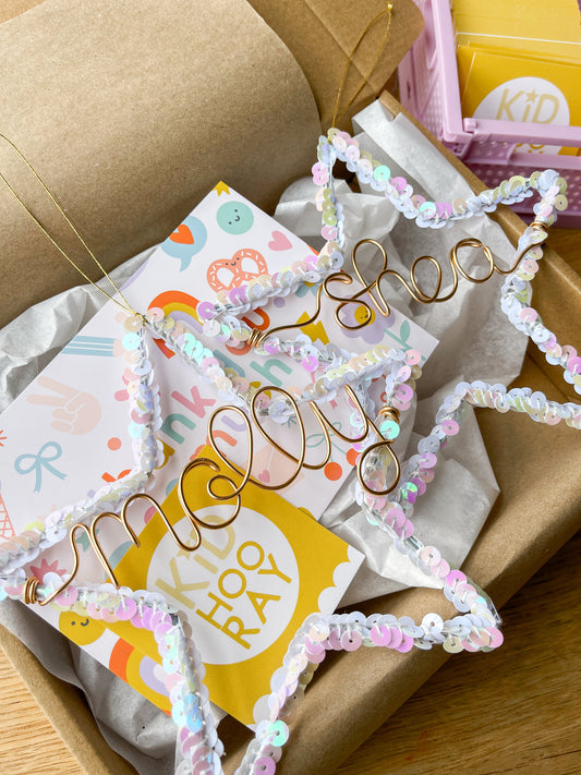 Personalized Christmas star ornaments in white sequins with gold wire names Molly and Shea, shown in gift packaging with close-up holiday detail.