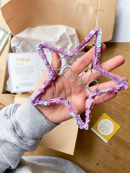 Hand holding a purple sequin star ornament personalized with the name Laila in gold wire, ready to package as a Christmas gift.