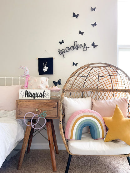 Black knitted wire word sign that spells ‘Spooky,’ styled as Halloween décor in a little girl’s bedroom. The sign hangs on the wall surrounded by black butterfly accents, creating a fun and festive seasonal touch. Perfect for decorating kids’ spaces for Halloween, this handmade yarn wall sign adds a spooky yet playful vibe to a child’s room, nursery, or playroom, making holiday decorating simple, stylish, and unique.