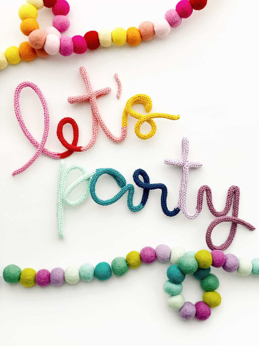 Knitted wire word "let's party" in rainbow color scheme.