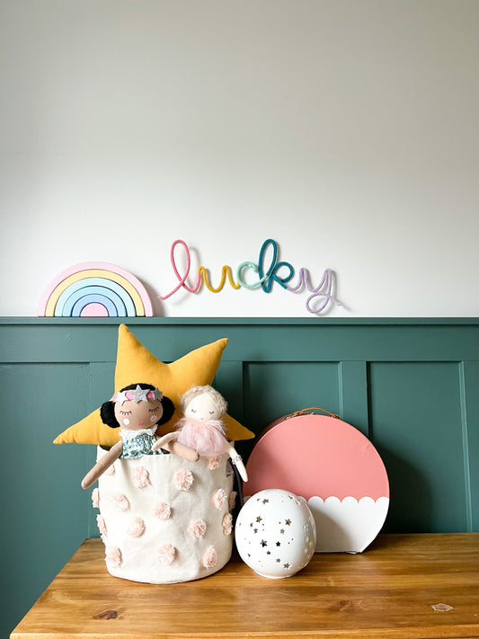 Knitted wire word lucky in rainbow color scheme. It's hung above a child's desk. 