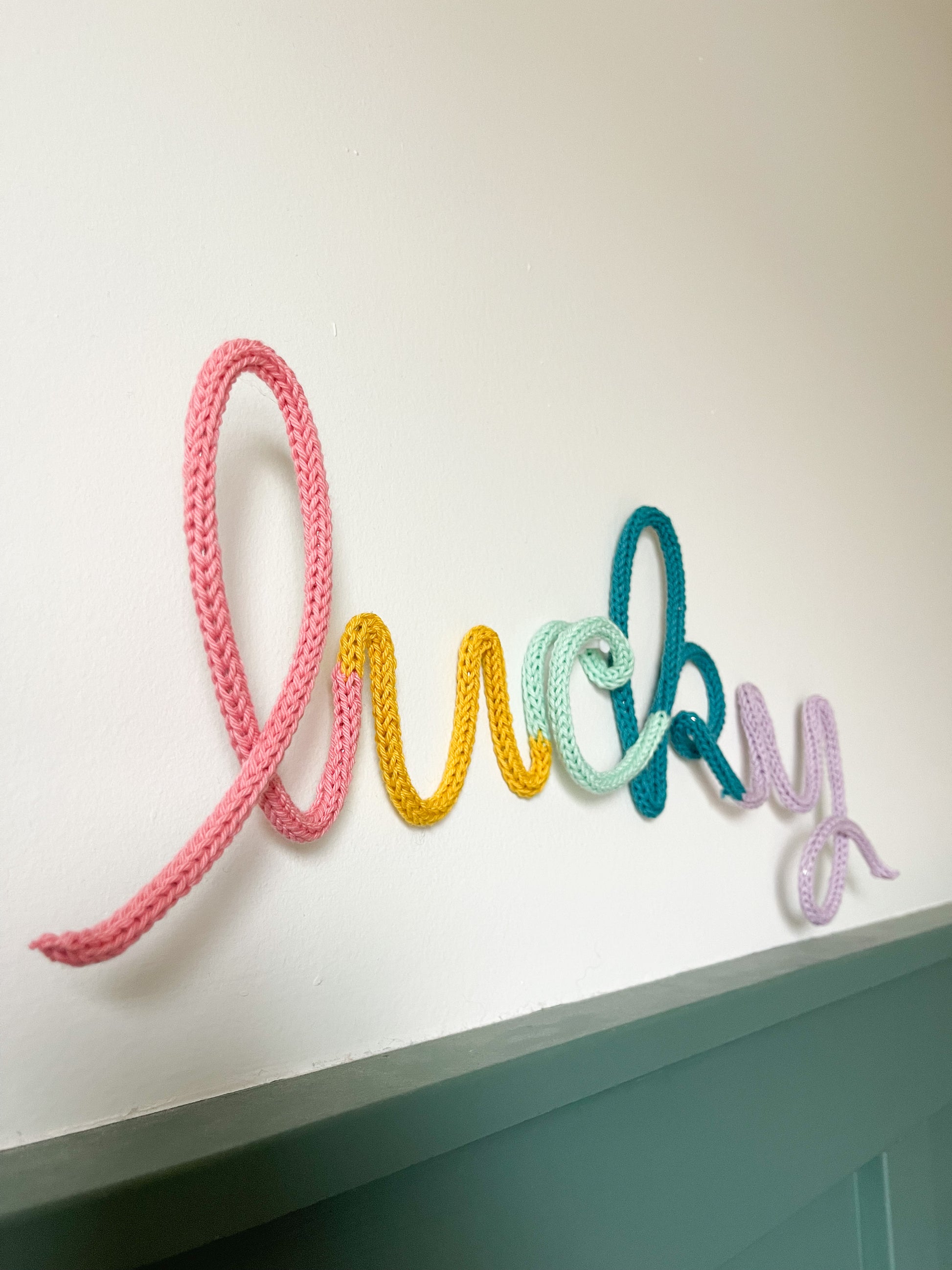 Knitted wire word "lucky" in rainbow color scheme.