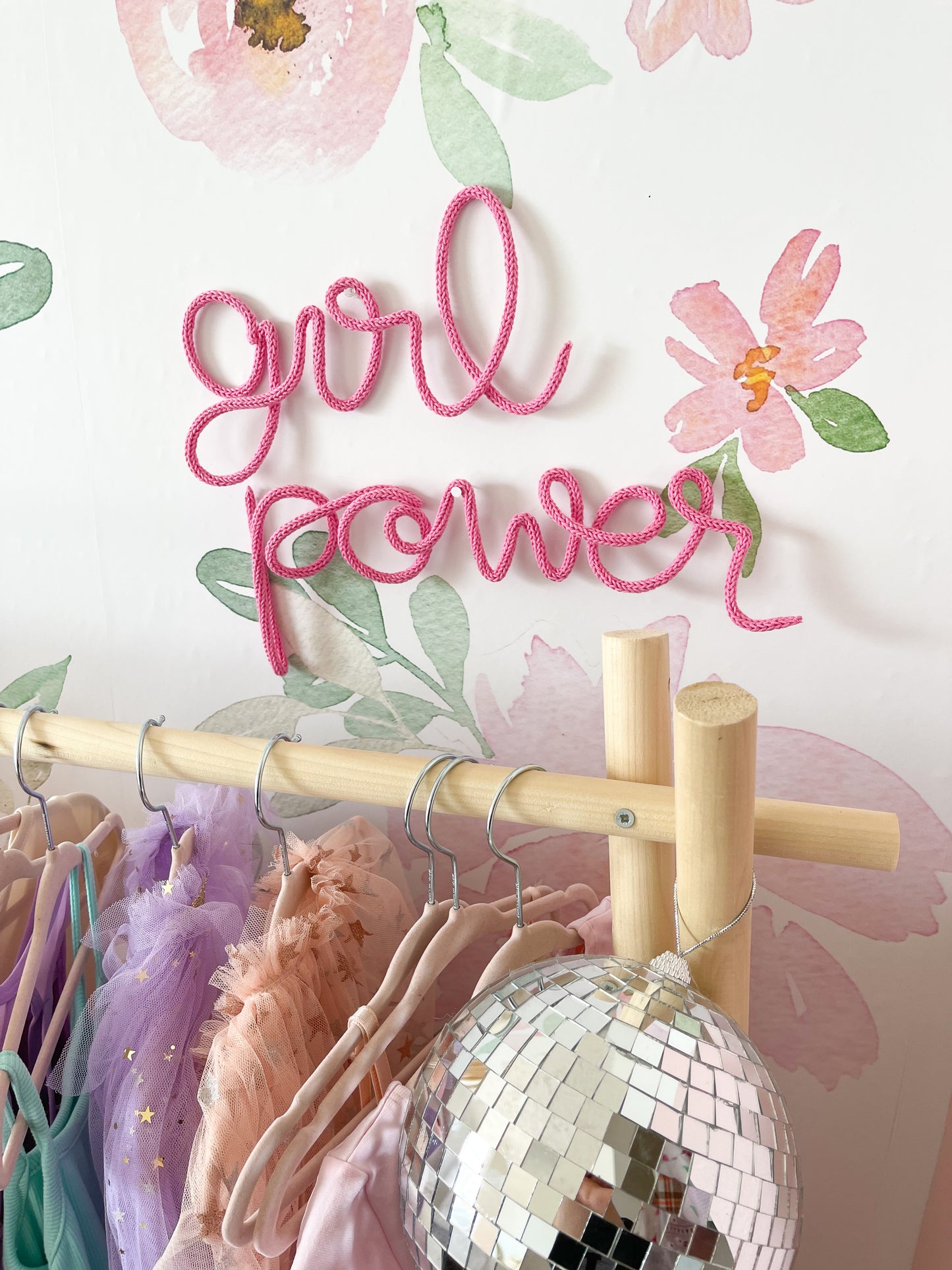 knitted wire word "girl power". It's hanging above a dress up rack in a girls bedroom. 