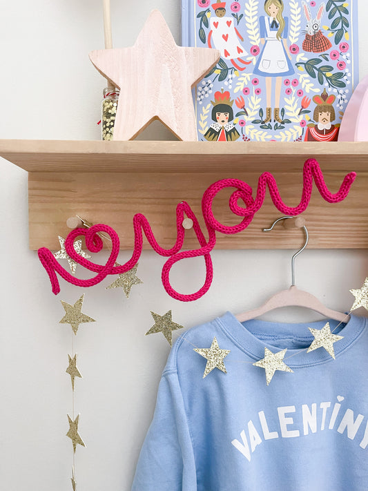 Knitted wire art "i heart you" sign featuring a vibrant neon pink color hanging on a styled peg rail in a kid's room.