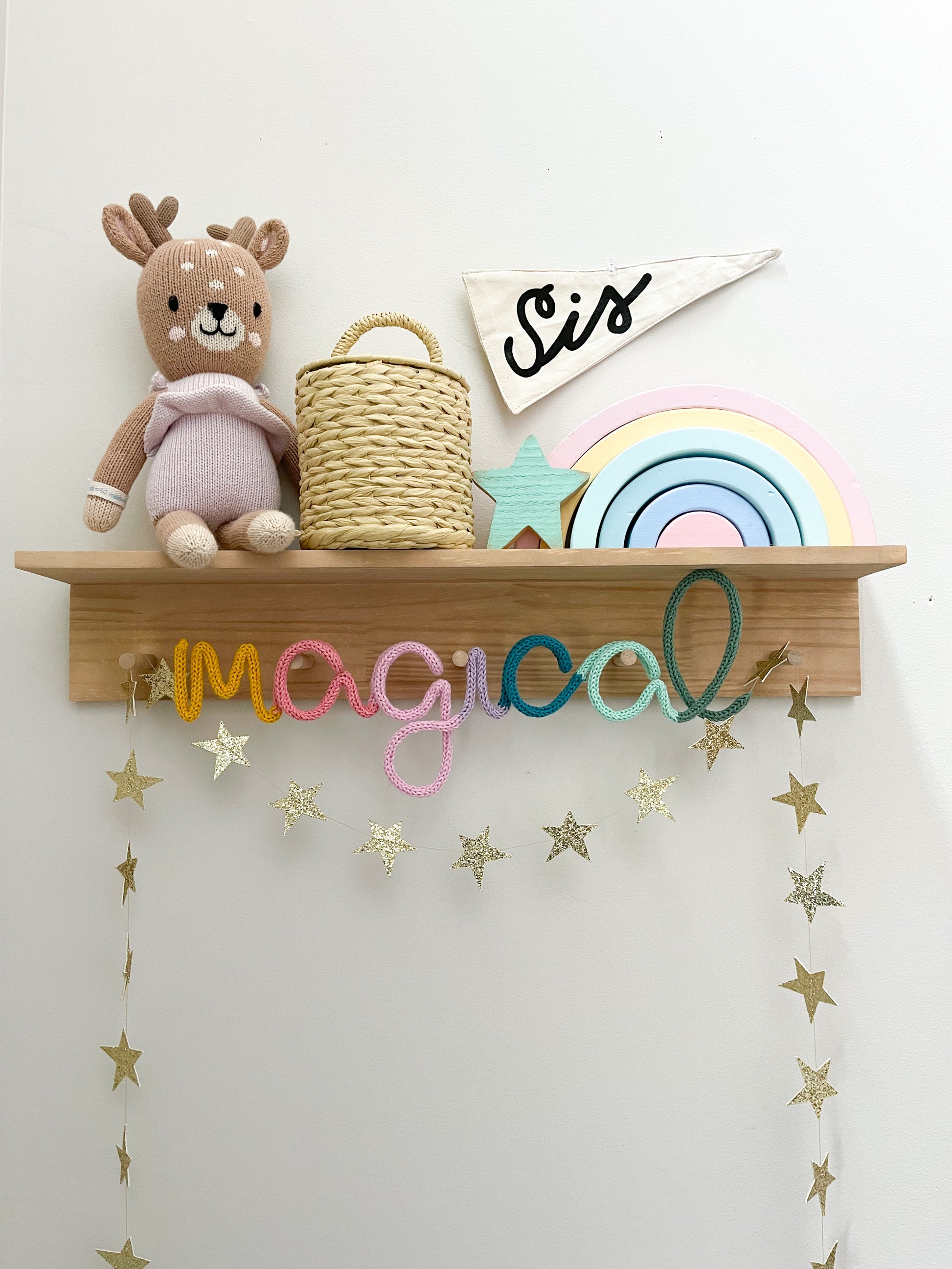 Knitted wire word "magical" in rainbow color scheme. It's styled on a peg rail shelf in a kid's space.