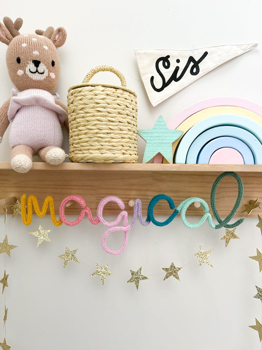 Knitted wire word "magical" in rainbow color scheme. It's styled on a peg rail shelf in a kid's space.