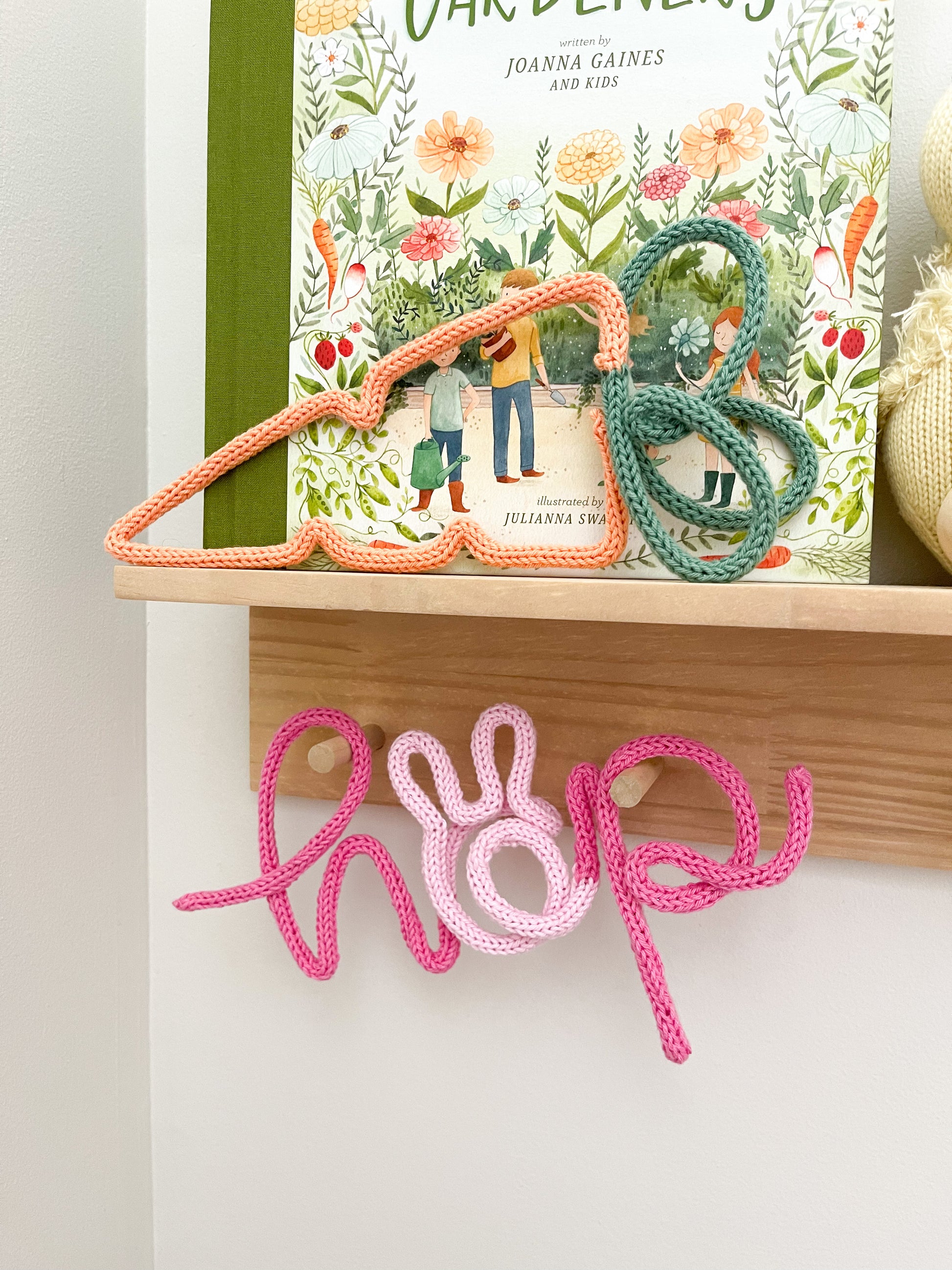 Knitted wire word "hop" featuring bunny ears. It's hanging on a peg rail styled shelfie.