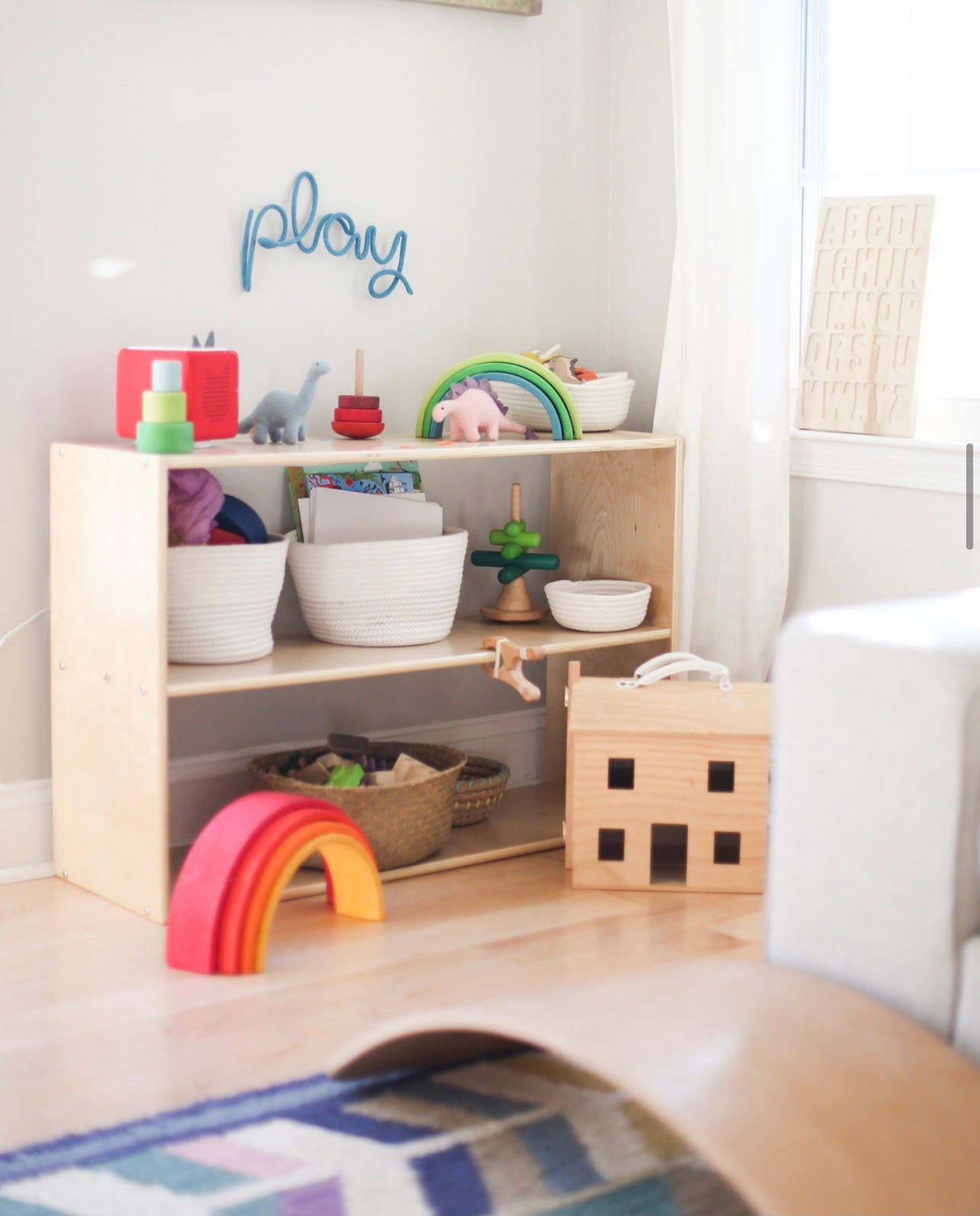 Knitted wire word "play" sign hung above toy storage in playroom. 