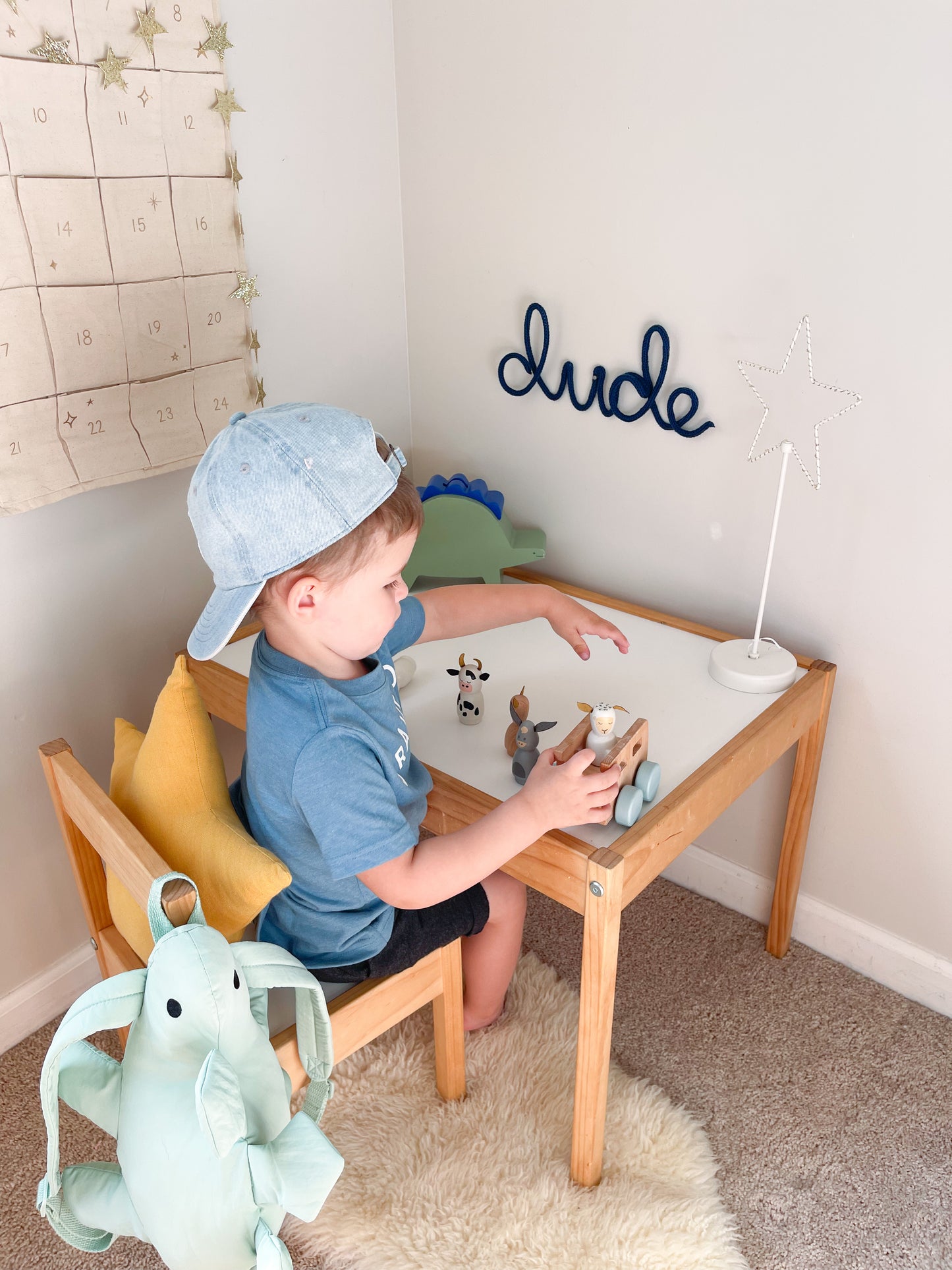 Knitted wire word "dude" sign. It's hung above a desk in a little boy's room. The boy is sitting at the desk playing with toys.