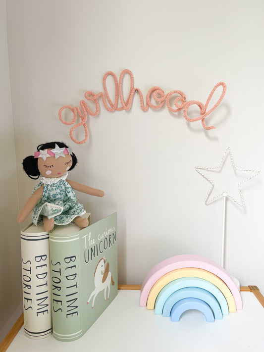 Knitted wire word "girlhood" sign. It's hanging above a girl's desk in her bedroom. 
