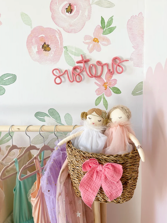 Knitted wire word "sisters" sign. It's hanging above a dress up rack in a girls bedroom. 